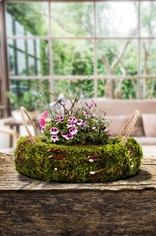 Handgefertigter Moos-Pflanzkorb mit dekorativen Kordeln, gefüllt mit einer Auswahl an natürlichen Materialien, präsentiert auf einem rustikalen Hintergrund.