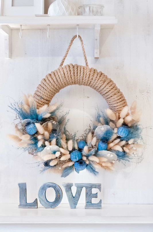 Handgefertigter Türkranz 'Blue Sea' mit blauen und neutralen Trockenblumen an einer hellen Wand – dekogreen.de