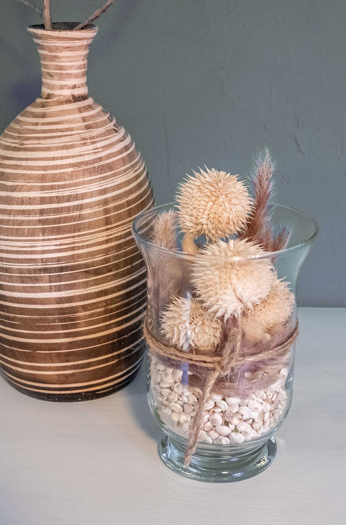 Handgefertigtes Trockenblumengesteck im Glas mit Distelköpfen und Muscheln auf weißem Hintergrund – dekogreen.de